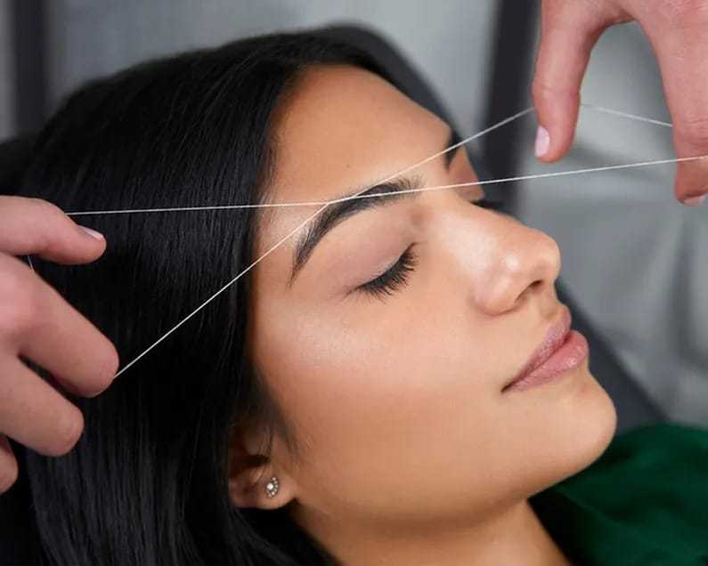 Young woman getting eyebrow threading treatment.