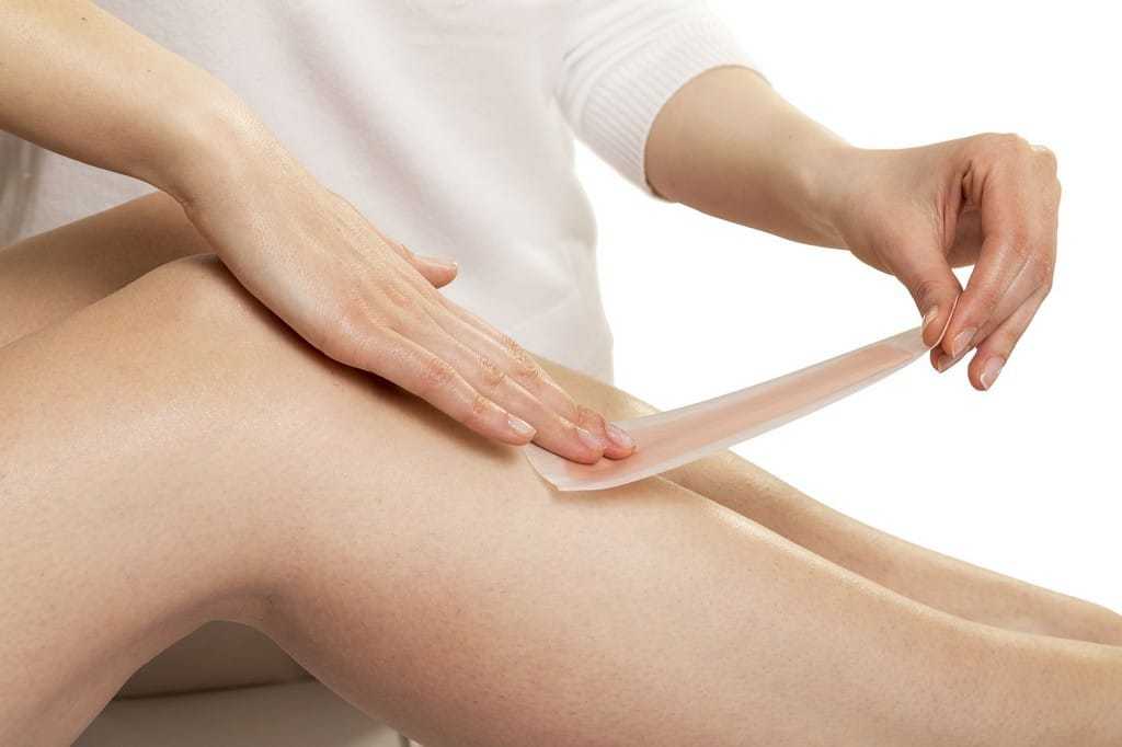 Woman applying a wax strip on her leg for hair removal.
