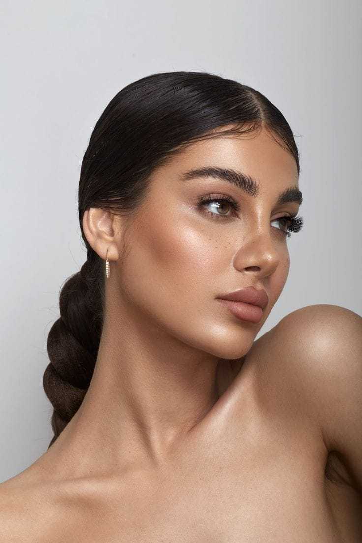 Young woman with slicked-back hairstyle and neutral makeup, looking to the side.